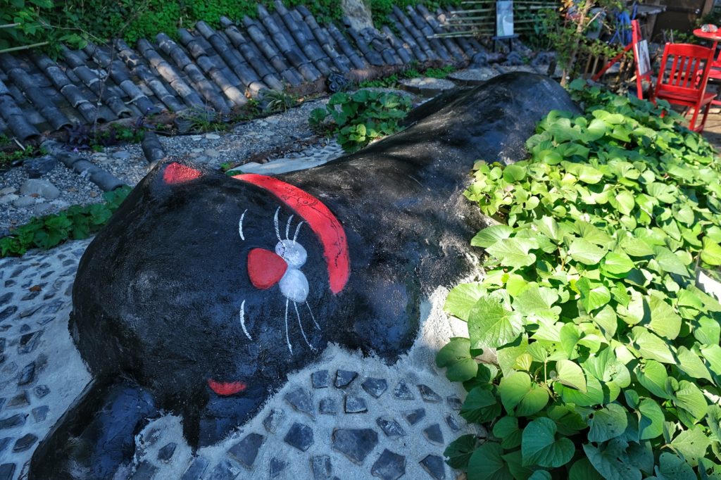 Un chat allongé rigolo en sculpture dans un curieux jardin de l'allée des chats d'Onomichi